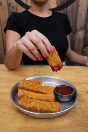 Photo for Gastronomy. Closeup view of woman's holding a fried mozzarella cheese stick dipped in a spicy sauce. - Royalty Free Image