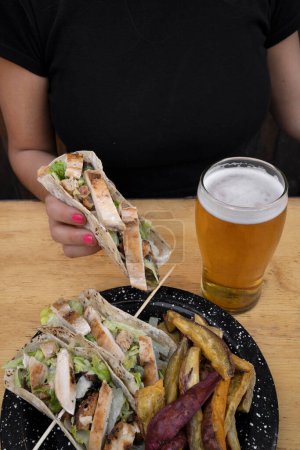 Photo for Having tacos and a pint of beer. Closeup view of a woman holding a taco with grilled chicken breast and lettuce. - Royalty Free Image