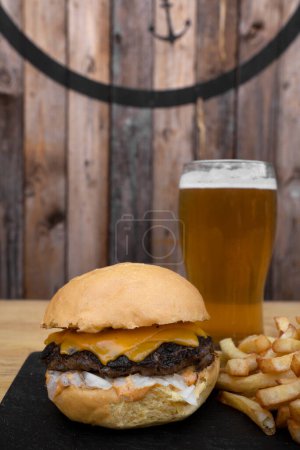 Téléchargez les photos : Cheeseburger traditionnel au cheddar, oignon, frites et un verre de bière. - en image libre de droit