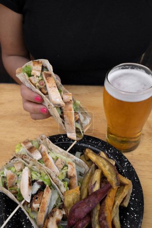 Téléchargez les photos : Des tacos et une pinte de bière. Vue rapprochée d'une femme tenant un taco avec poitrine de poulet grillée et laitue. - en image libre de droit