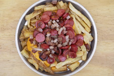 Photo for Fries. Top view of fried potatoes with sliced sausages and crispy bacon, in a metal dish with a wooden background. - Royalty Free Image