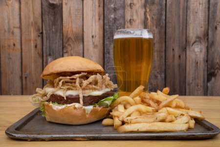 Photo for Plant based burger. Not Burger. Closeup view of NotCo hamburger with lettuce, crispy onion rings, cheese, NotCo mayo a pint of beer and fried potatoes. - Royalty Free Image