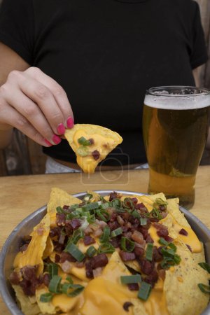 Téléchargez les photos : Manger des nachos. Vue rapprochée d'une femme tenant un nacho au fromage cheddar, oignon vert et bacon croustillant. - en image libre de droit