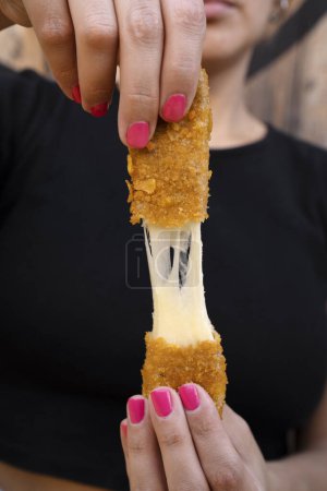Woman stretching fried mozzarella cheese sticks.