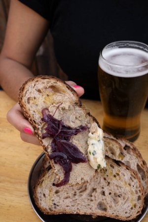 Foto de Antipasti. Vista de cerca de una mujer sosteniendo una tostada de pan de centeno con paté, cebollas glaseadas y queso azul. - Imagen libre de derechos