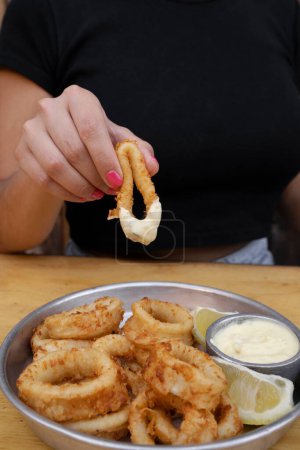 Foto de Comer mariscos. vista de cerca de la mano de una mujer sumergiendo un anillo de calamar frito en salsa aioli. - Imagen libre de derechos