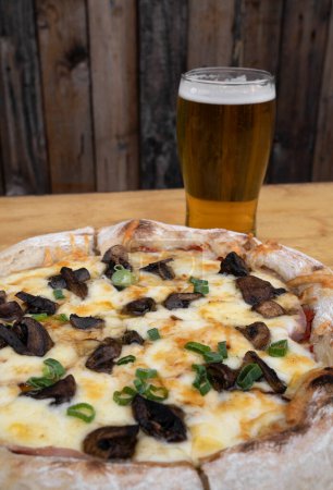Téléchargez les photos : Pizza et bière. Vue rapprochée d'une pizza avec provolone et fromage mozzarella, sauce tomate et champignons, et une pinte de bière. - en image libre de droit
