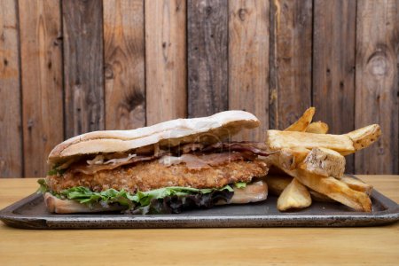 Téléchargez les photos : Sandwich gourmand. Vue rapprochée d'un sandwich multicouche avec steak au poulet frit, bacon, fromage et laitue, avec pommes de terre frites. - en image libre de droit