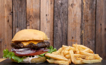 Téléchargez les photos : Restauration rapide. Vue rapprochée d'un hamburger avec laitue, tomate, fromage cheddar, oignon rouge, mayonnaise et frites. - en image libre de droit