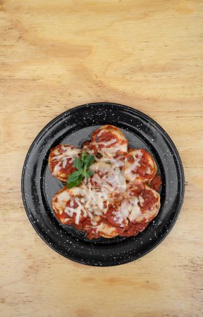 Pastas rellenas. Vista superior de los sorrentinos con salsa de tomate mediterráneo y queso provolone en un plato negro sobre la mesa de madera.