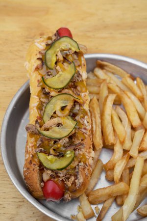 Foto de Hot dog con cebolla crujiente, pepino en rodajas y mostaza con miel, con papas fritas en un plato de metal. - Imagen libre de derechos