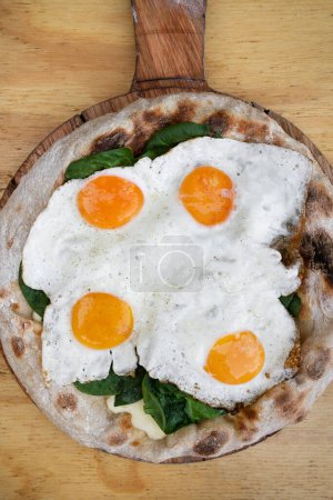 Photo for Top view of a pizza with mozzarella cheese, spinach and fried eggs, on the wooden table. - Royalty Free Image