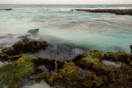 Foto de Atardecer en la playa tropical de la bahía. Long exposure shot of the turquoise color sea, blurred ocean waves and rocks in Tulum, México. - Imagen libre de derechos