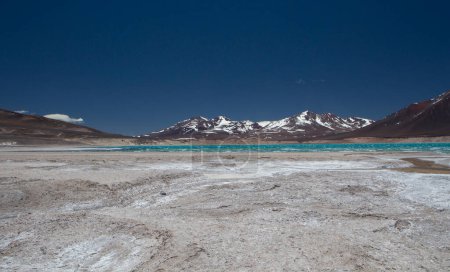 Foto de Paisaje alpino en la cordillera. Hermoso lago de agua de glaciar turquesa en lo alto de la cordillera de los Andes rodeado de salinas naturales y montañas volcánicas bajo un cielo azul profundo. - Imagen libre de derechos