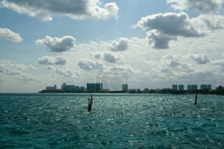 Téléchargez les photos : Vue depuis un bateau naviguant sur l'océan d'eau turquoise. La mer bleue, le littoral et les bâtiments de la ville de Cancun à l'horizon, par une journée d'été ensoleillée. - en image libre de droit