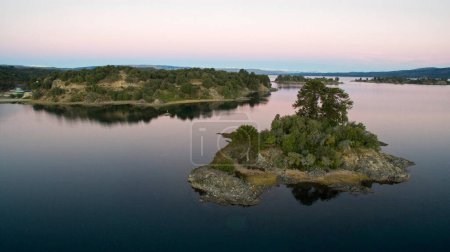 Foto de El lago al anochecer. Hermosa vista aérea de una isla, el lago, la costa, el reflejo en el agua y el bosque al anochecer. - Imagen libre de derechos