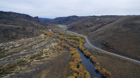 Foto de Paisaje idílico. Vista aérea de la carretera rural y el arroyo, que fluye a través del prado amarillo, valle y montañas. - Imagen libre de derechos