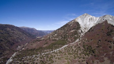 Foto de Colores otoñales. Vista aérea de la colina Impodi con un pico de granito blanco, árboles Araucaria araucana follaje forestal, montañas y camino de tierra a través del valle. - Imagen libre de derechos