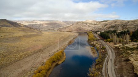 Photo for Idyllic landscape. Traveling along the rural dirt road. Aerial view of a stream flowing across the golden meadow, valley and mountains. The sky reflection in the water. - Royalty Free Image