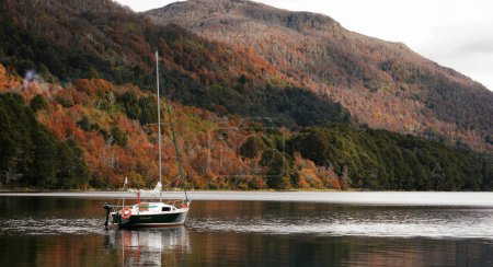 Photo for Autumn colors, Sailboat on the calm water of the lake, surrounded by mountains and forest in autumn - Royalty Free Image