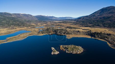 Téléchargez les photos : Vue aérienne du lac d'eau bleue pure, d'un îlot, de la vallée dorée, du littoral, de la prairie et des montagnes par une journée d'été ensoleillée. - en image libre de droit