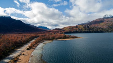 Traveling along the road in the woods. Aerial view of the blue water lake, beach, mountains and forest in autumn. 