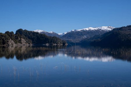 Foto de Vista del volcán Batea Mahuida, cordillera de los Andes, bosque y lago de alúmina en Villa Pehuenia, Patagonia Argentina. Hermoso paisaje y reflejo del cielo azul en el agua del glaciar. - Imagen libre de derechos