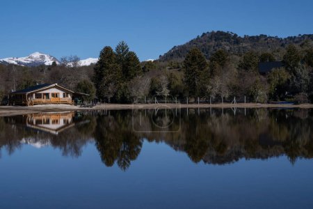 Téléchargez les photos : La maison du lac par une journée ensoleillée. Vue de la cabane, de la forêt, des montagnes et du ciel bleu reflet à la surface de l'eau. - en image libre de droit