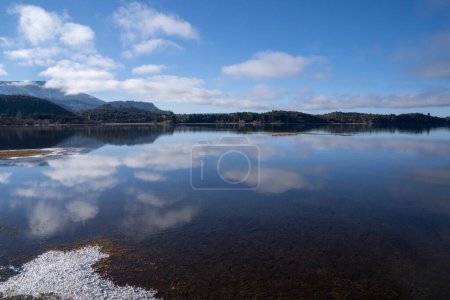 Téléchargez les photos : Le lac calme dans une matinée ensoleillée. Vue panoramique sur la forêt, le lac et le reflet parfait du ciel dans l'eau bleue. La chaîne de montagnes des Andes en arrière-plan. - en image libre de droit