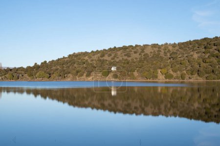 Téléchargez les photos : Des vacances. Vue sur la maison du lac dans la colline à côté du lac. Le ciel bleu, la forêt et les montagnes se reflètent dans l'eau. - en image libre de droit