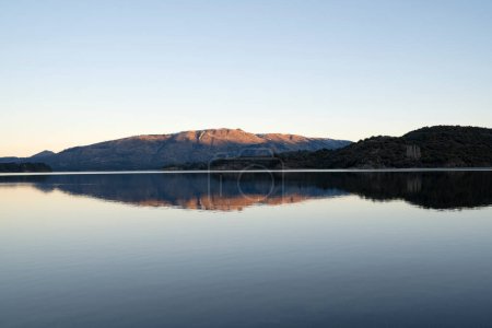 Téléchargez les photos : Vue enchanteresse sur le lac placide au coucher du soleil. Les montagnes, la forêt et le ciel bleu se reflètent dans l'eau. - en image libre de droit