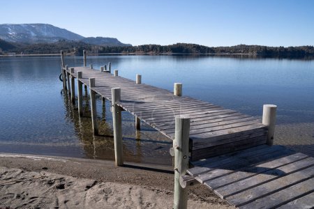 Photo for The wooden docks in the calm lake. The clear blue sky and pier reflected in the water surface. The forest and mountains in the background. - Royalty Free Image