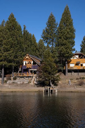 Photo for Lake house. View of the wooden cabins built besides the placid lake.  The beautiful green forest and blue sky reflection in the water. - Royalty Free Image