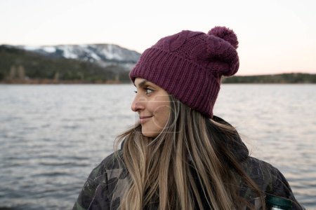 Téléchargez les photos : Portrait d'une jeune femme souriante. Le lac placide et la chaîne de montagnes en arrière-plan. Belles couleurs de coucher de soleil dans l'environnement. - en image libre de droit