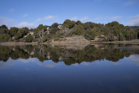 Photo for Panorama view of the wooden lake houses in the forest. The shoreline, wood, cliffs, and blue sky reflection in the water. - Royalty Free Image