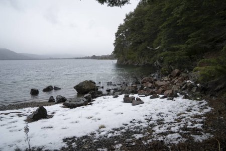 Téléchargez les photos : Le lac en hiver dans une matinée nuageuse. Le rivage rocheux avec neige, forêt et montagnes au lever du soleil. - en image libre de droit