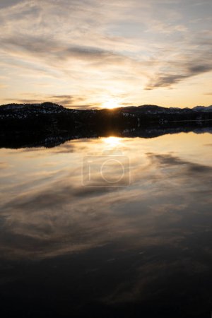 Téléchargez les photos : Coucher de soleil magique dans le lac. Vue panoramique sur le lac aux palourdes, soleil caché et ciel spectaculaire avec nuages, beau reflet à la surface de l'eau. La forêt et les montagnes à l'horizon. - en image libre de droit