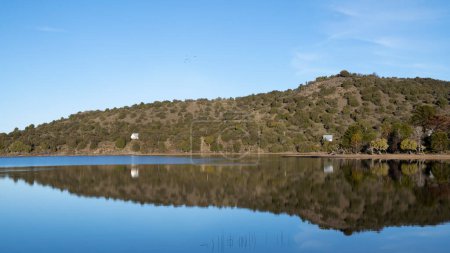 Téléchargez les photos : Symétrie dans la nature. Vue panoramique sur le lac calme. Les collines, la forêt verte et le reflet bleu clair du ciel à la surface de l'eau. - en image libre de droit