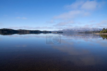 Téléchargez les photos : Le lac par une matinée ensoleillée. Vue panoramique sur la forêt, le lac et le reflet parfait du ciel dans l'eau bleue. La chaîne de montagnes des Andes en arrière-plan. - en image libre de droit