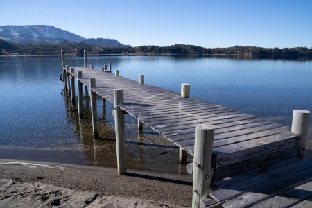 Téléchargez les photos : Le rivage de la plage et quai en bois dans le lac placide. Vue du ciel bleu, de la forêt et des montagnes reflet dans l'eau. - en image libre de droit