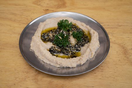 Foto de Cocina de Oriente Medio. Vista de cerca de hummus dip tradicional, hecho con garbanzos, en un plato de metal en la mesa de madera. - Imagen libre de derechos