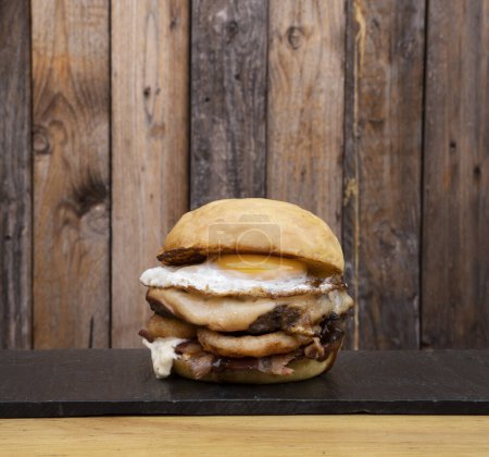 Téléchargez les photos : Burger multicouche avec viande grillée, fromage provolone, rondelles d'oignon bacon, sauce barbecue et un œuf grillé. - en image libre de droit
