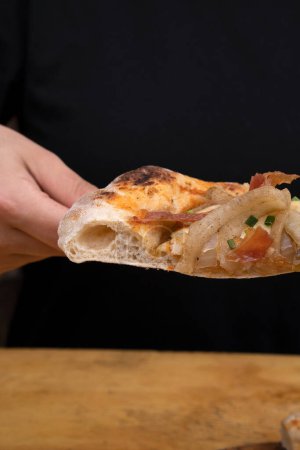 Foto de Comiendo pizza. Vista de cerca de la mano de una mujer que sirve una rebanada de pizza con salsa de tomate, queso mozzarella, tocino crujiente y cebolla, en la mesa de madera. - Imagen libre de derechos