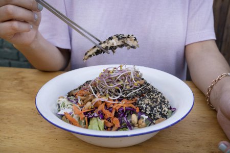 Photo for Food presentation. Closeup view of a woman presenting a salad made with carrot, lettuce, peanuts, chicken breast breaded with seeds, soy sprouts and cabbage, in a white bowl. - Royalty Free Image