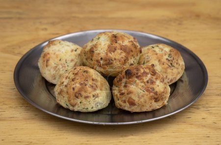 Photo for Closeup view of small, baked, cheese-flavored rolls, called chipa, in a metal dish with a wooden background. - Royalty Free Image