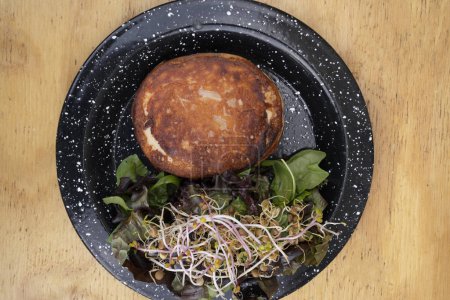 Téléchargez les photos : Vue de dessus d'un fromage provolone grillé, également appelé provoleta, avec une salade verte fraîche, dans un plat noir sur la table en bois. - en image libre de droit