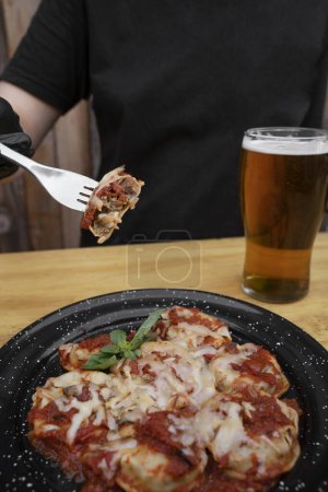 Photo for Stuffed pasta. Closeup view of a hand holding a fork, eating sorrentinos stuffed with cherry tomatoes and veal, with a mediterranean sauce and provolone cheese. - Royalty Free Image