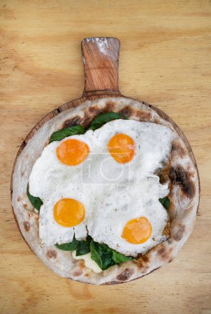 Photo for Top view of a pizza with mozzarella cheese, spinach and fried eggs, on the wooden table. - Royalty Free Image