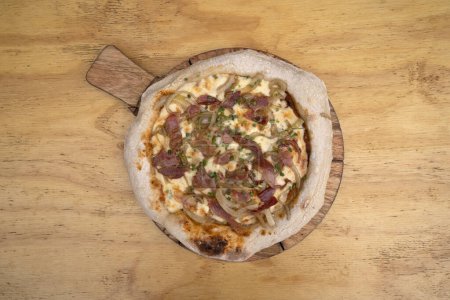 Foto de Vista superior de una pizza hecha con salsa de tomate, queso mozzarella, tocino crujiente y cebolla, con fondo de madera. - Imagen libre de derechos