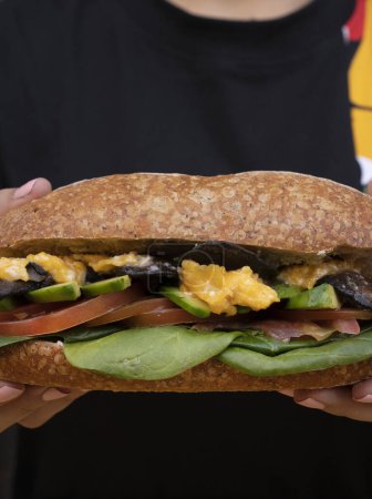 Téléchargez les photos : Femme tenant un délicieux sandwich fait avec du pain baguette, avocat, épinards, tomate et champignons. - en image libre de droit